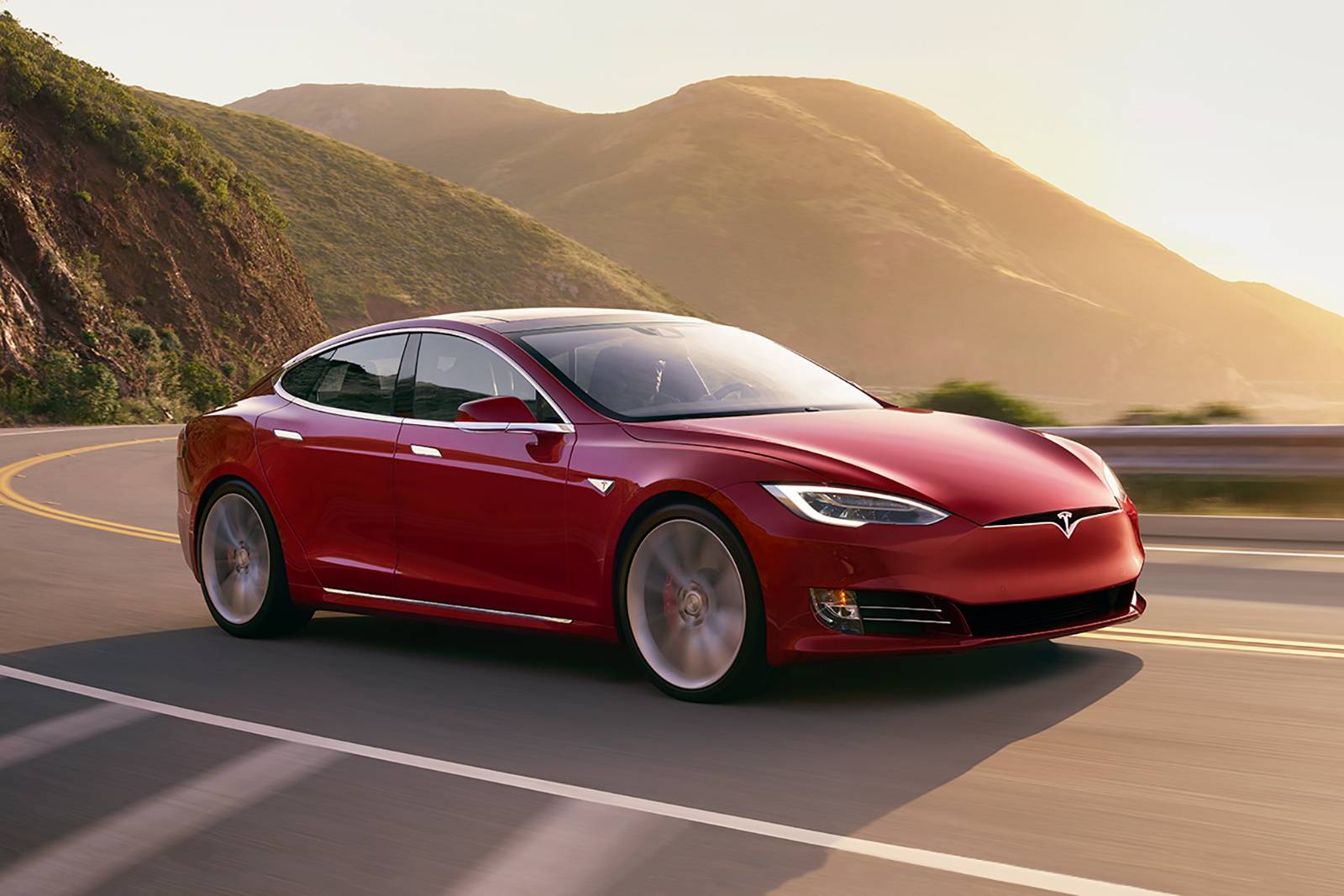 A red Tesla Model S driving in a road by the mountains
